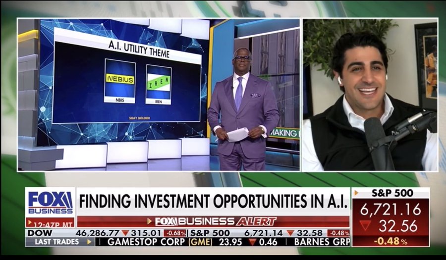 A screenshot from a Fox Business news broadcast titled Finding Investment Opportunities in AI features a split-screen format with market data on the right side displaying indices like S and P 500 at 6211.16 up 1.72 percent Dow at 42867.03 up 1.05 percent Nasdaq at 20071.04 up 2.35 percent and individual stocks such as GameStop Corp at 23.75 up 0.40 and Barnes Group at 0.48 down 0.32. The left side shows two men in a studio one in a purple suit standing at a desk with an AI Utility Theme graphic highlighting M E B and E T and the other seated wearing a beige vest speaking into a microphone with a neutral background. The overall composition includes news tickers at the bottom and branding elements for Fox Business.
