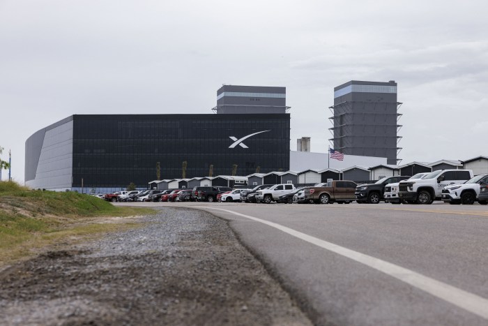 SpaceX's production facility and office building at its headquarters in Starbase, Texas, with a parking lot full of vehicles in the foreground.