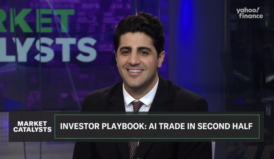 A man in a dark suit and tie sits in a studio with blue lighting behind him wearing a friendly smile during a broadcast segment labeled Market Catalysts with text overlay Investor Playbook: AI trade in second half and Yahoo Finance branding visible on screen