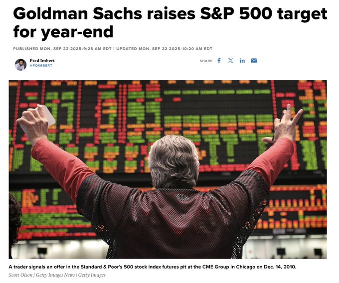 A person with gray hair wearing a red and black jacket stands with arms raised in a trading pit. Digital screens displaying stock market data are visible in the background. The text "Goldman Sachs raises S&P 500 target" is overlaid on the image.