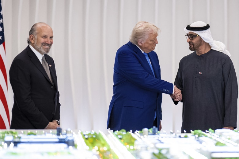US President Donald Trump and UAE President Sheikh Mohamed bin Zayed al-Nahyan shake hands in front of a model of the UAE USA AI Cluster, with US Secretary of Commerce Howard Lutnick looking on.