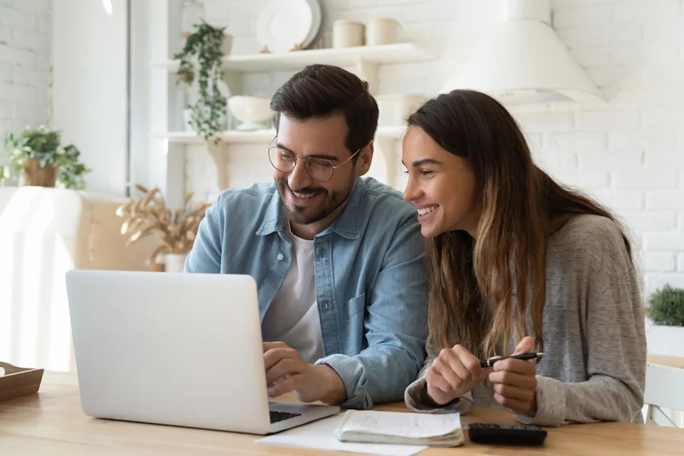 Two investors smile while working on a laptop in a living room.