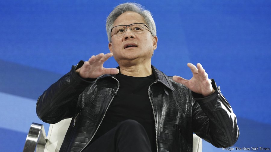 An older Asian man with gray hair and glasses wearing a black leather jacket over a black shirt sits on a white chair on a blue stage with his hands raised expressively as if speaking or gesturing during a presentation. The background includes a blue gradient and stage elements. A New York Times watermark appears in the bottom right corner.
