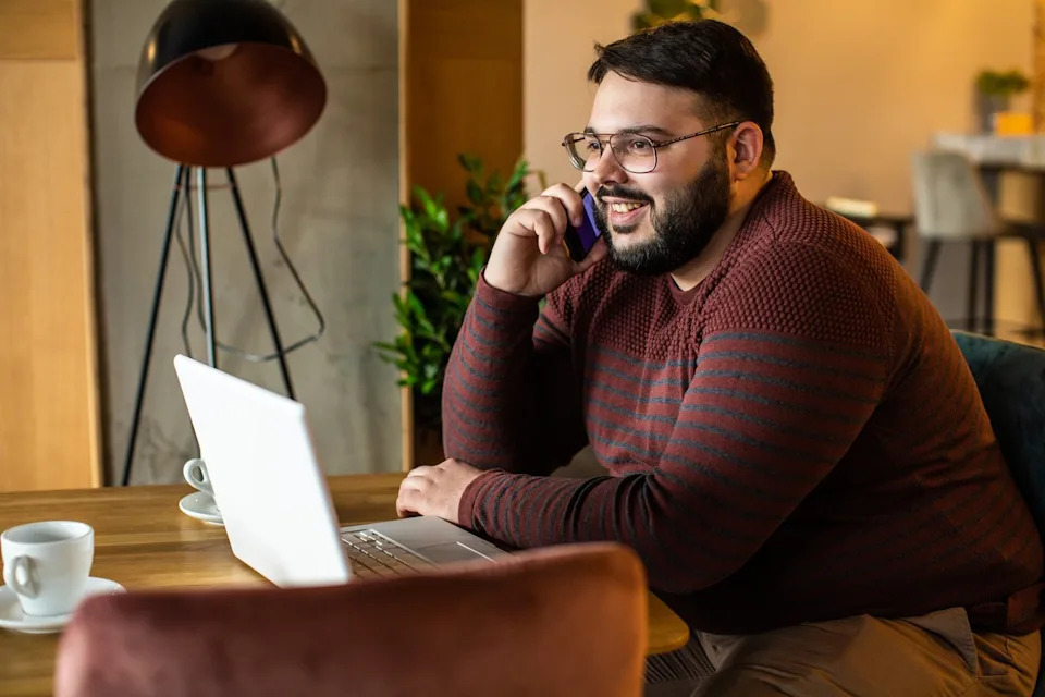 A person talks on the phone while sitting at a computer.