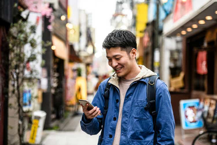 Cheerful young man looking at smartphone in street